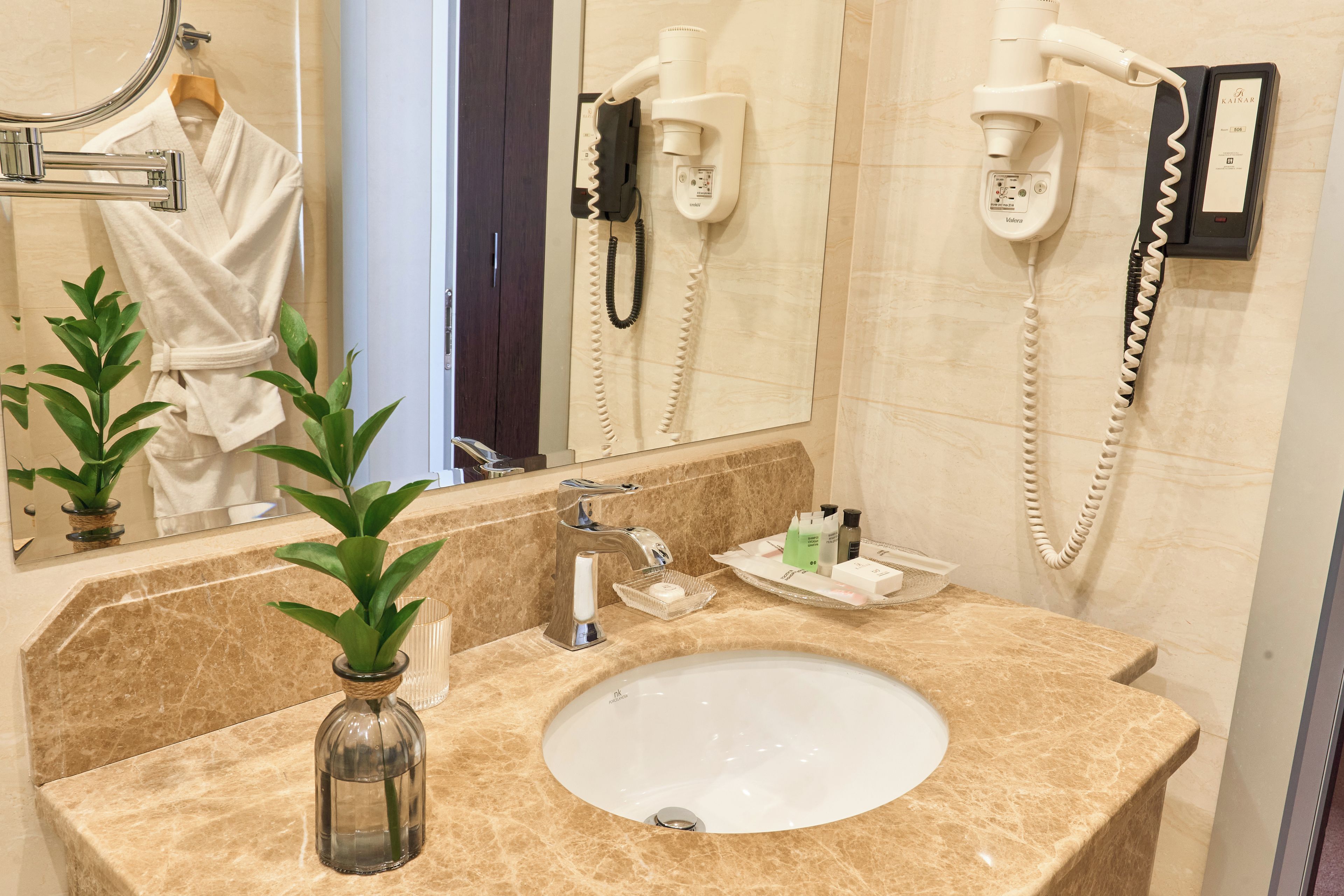 A bathroom with a marble sink, a hairdryer, and a robe hanging on the wall.