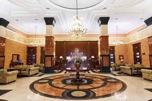 A lobby with a grand chandelier, a reception desk, and multiple seating areas. - Kainar Hotel (Shymkent)