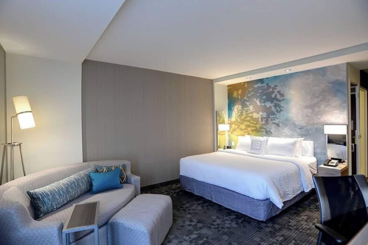 A hotel room with a large bed, a smaller sofa, a desk, and a painting on the wall.