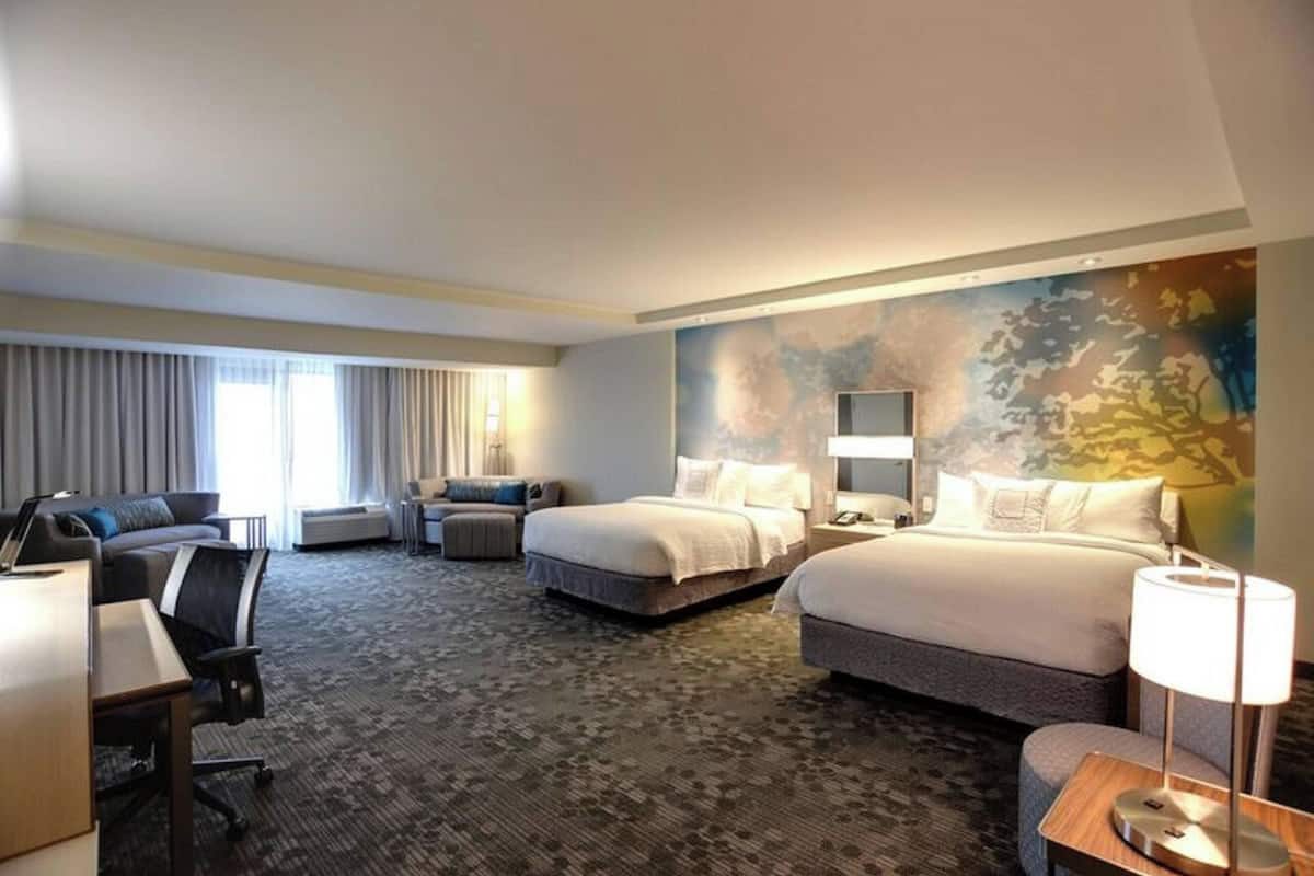 A hotel room with two beds, a desk, a chair, and a large window with curtains.
