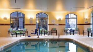 Un espace piscine avec des chaises et des tables, une piscine agrémentée d’un panneau indiquant qu’il est interdit de plonger, et de grandes fenêtres offrant une vue panoramique.
