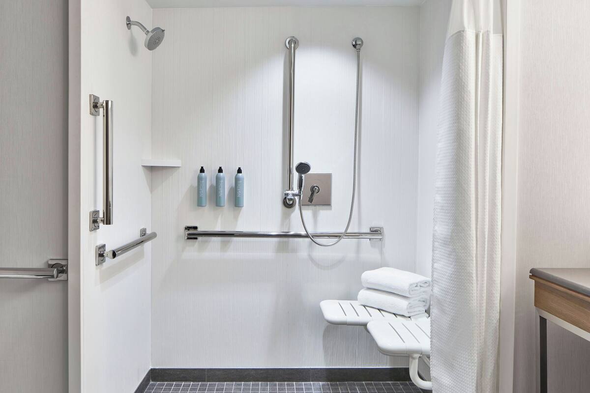 A modern bathroom with a walk-in shower, grab bars, a bench, and a towel rack.