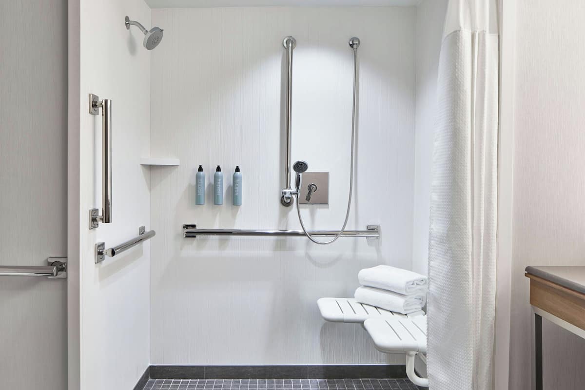 A modern bathroom with a walk-in shower, grab bars, a bench, and a towel rack.