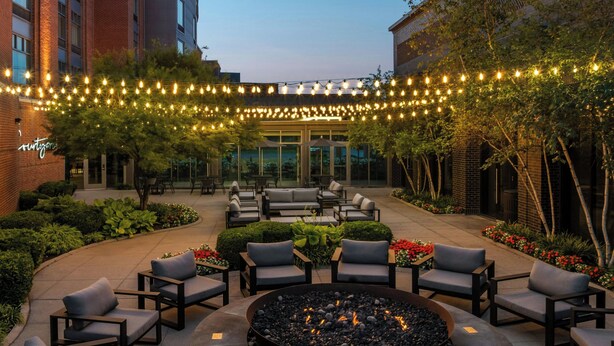 Un espace extérieur aménagé avec des sièges, un foyer, des chaises et des tables, le tout illuminé par des guirlandes lumineuses.