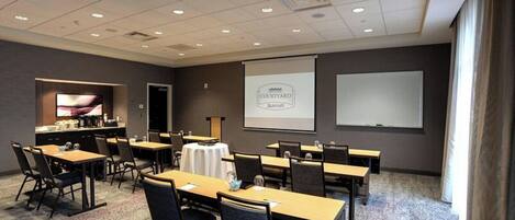 Un salón de conferencias con una pantalla grande, varias mesas y sillas, que muestra el logotipo de Marriott.