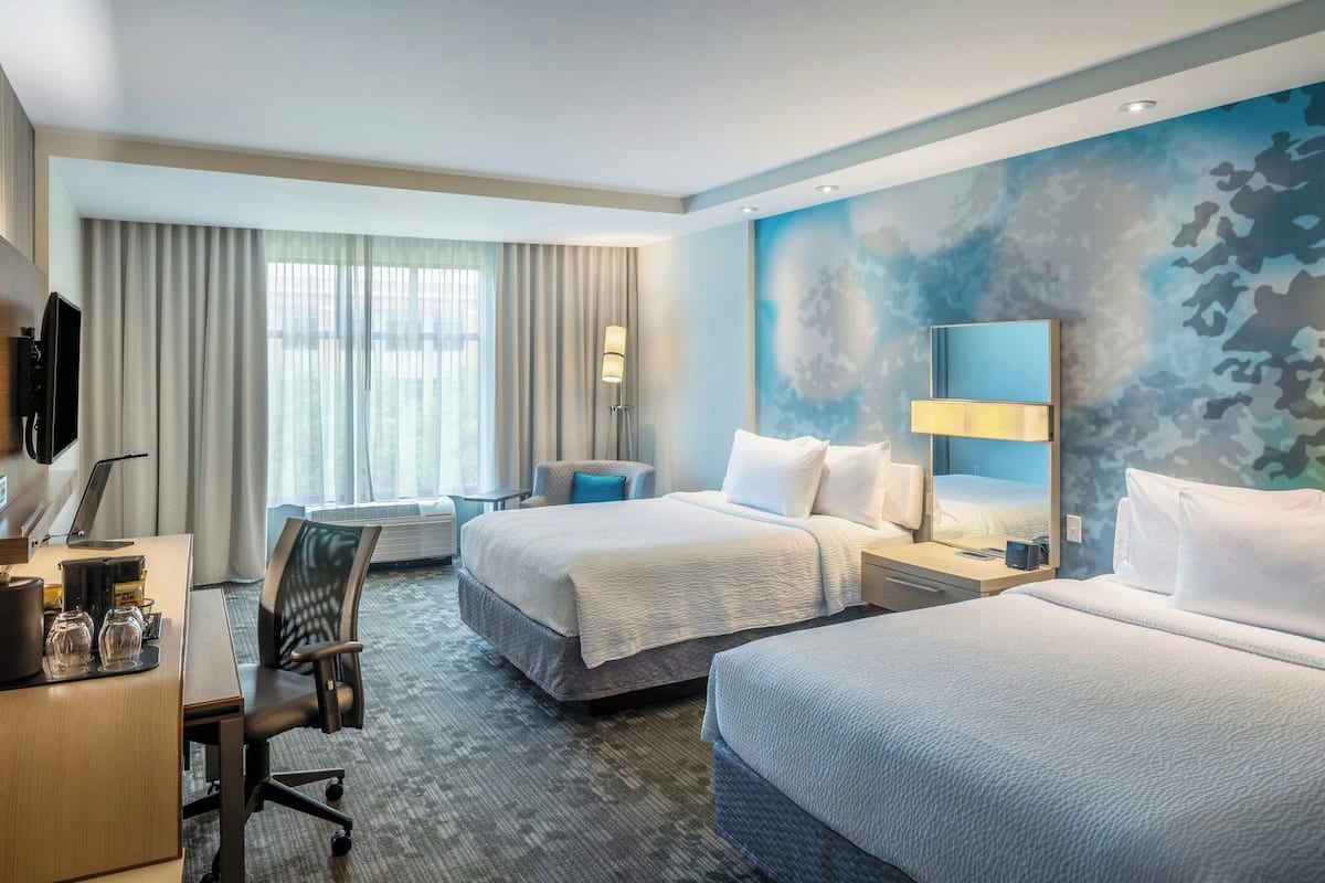 A hotel room with two beds, a desk with a computer, a chair, and a large window with curtains.