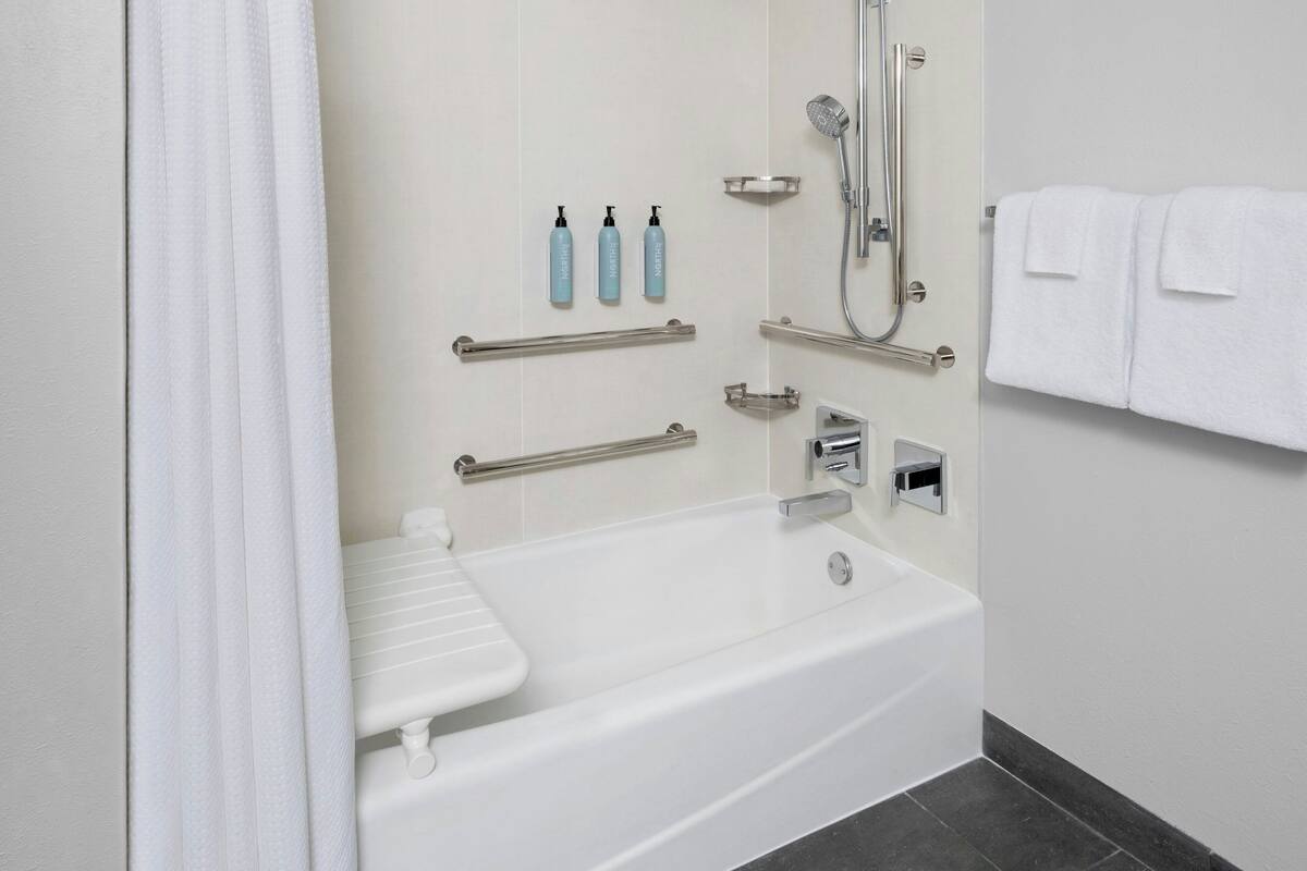 A modern bathroom with a white bathtub, grab bars, a handheld showerhead, and a towel rack.