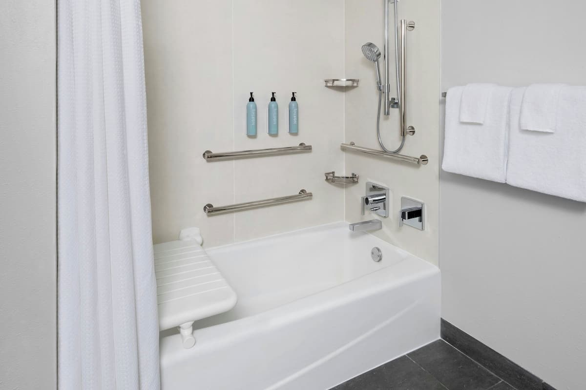A modern bathroom with a white bathtub, grab bars, a handheld showerhead, and a towel rack.