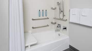 Un baño moderno con una bañera blanca, barras de apoyo, un cabezal de ducha manual y un perchero para toallas.