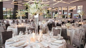 Une salle de banquet avec des tables rondes dressées pour un événement formel, agrémentée de grands vases remplis de fleurs et de bougies.
