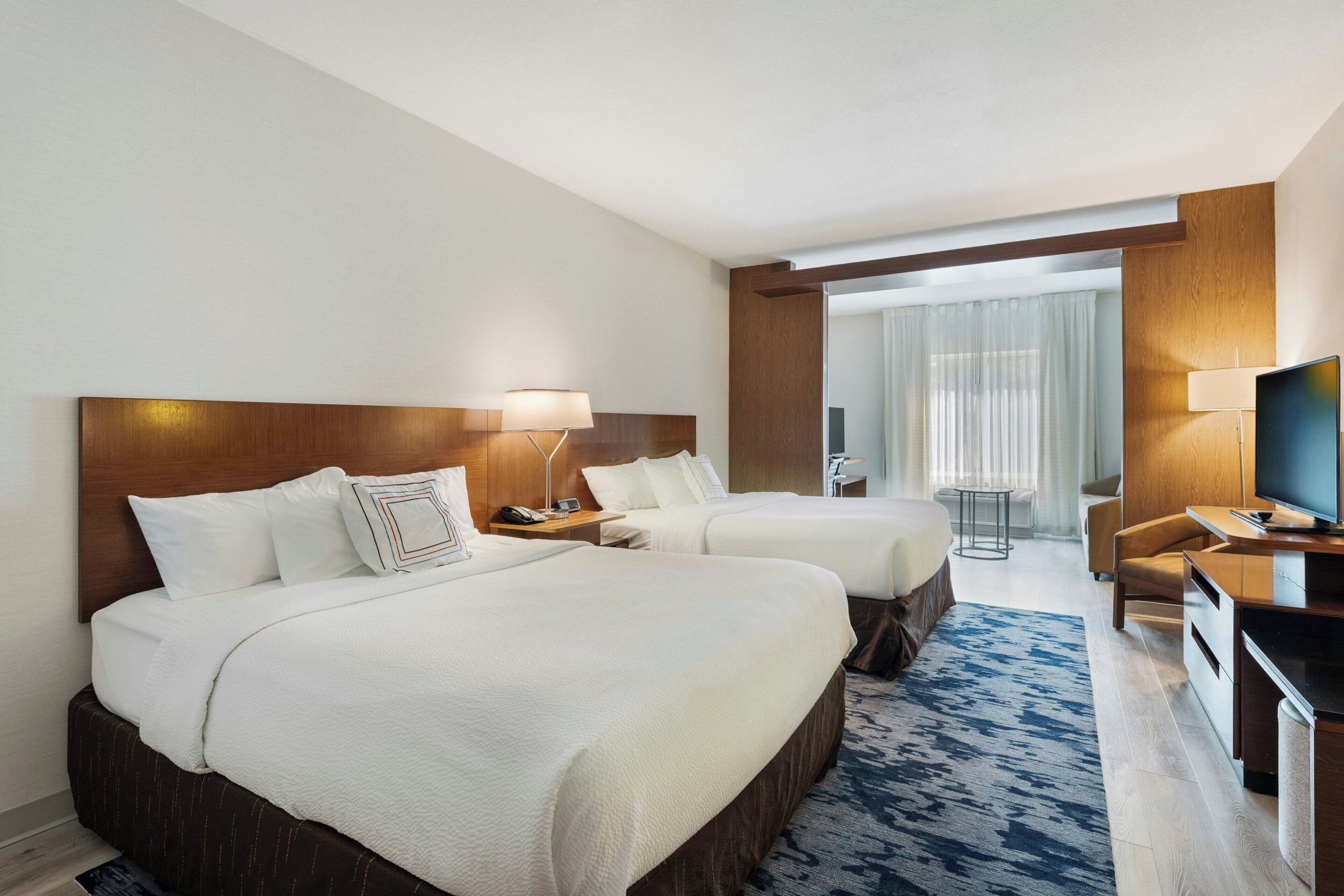 Quarto de hotel com duas camas, uma escrivaninha, uma TV e vista para uma varanda.