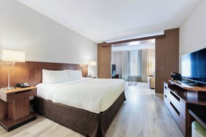 Une chambre d’hôtel avec un grand lit, des tables de chevet, un bureau avec une chaise, une télévision et une vue sur la pièce.