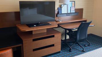 A hotel room with a wooden desk, a television, a lamp, and a patterned carpet.
