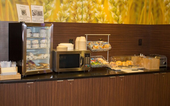 A buffet setup with a microwave, paper cups, and various food items. - Fairfield Inn & Suites by Marriott Geneva Finger Lakes (Geneva)