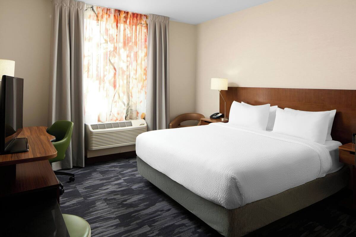 A hotel room with a large bed, a desk with a chair, a TV, and a window with curtains.