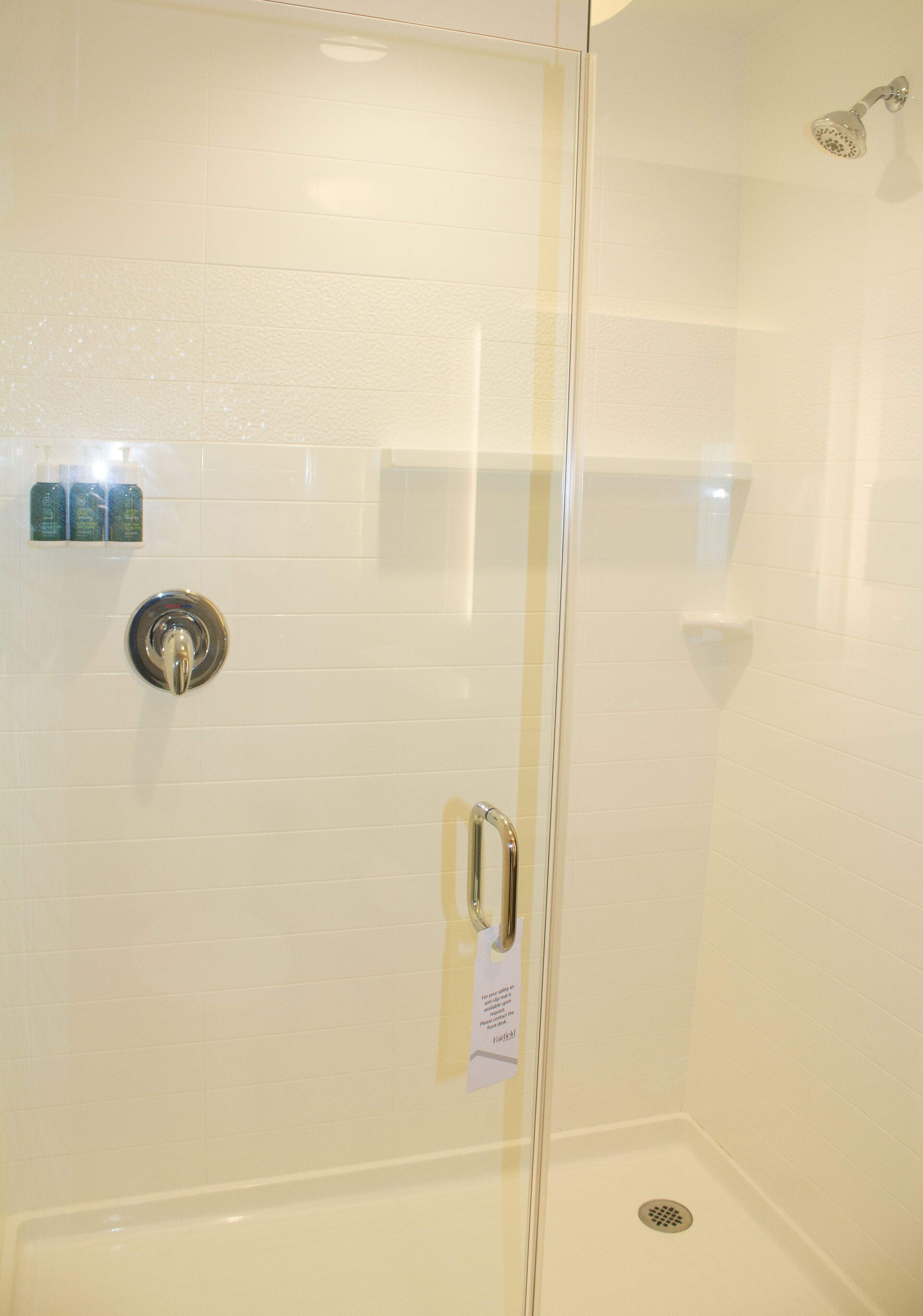 A glass-enclosed shower stall with a chrome showerhead, a control knob, and a drain.