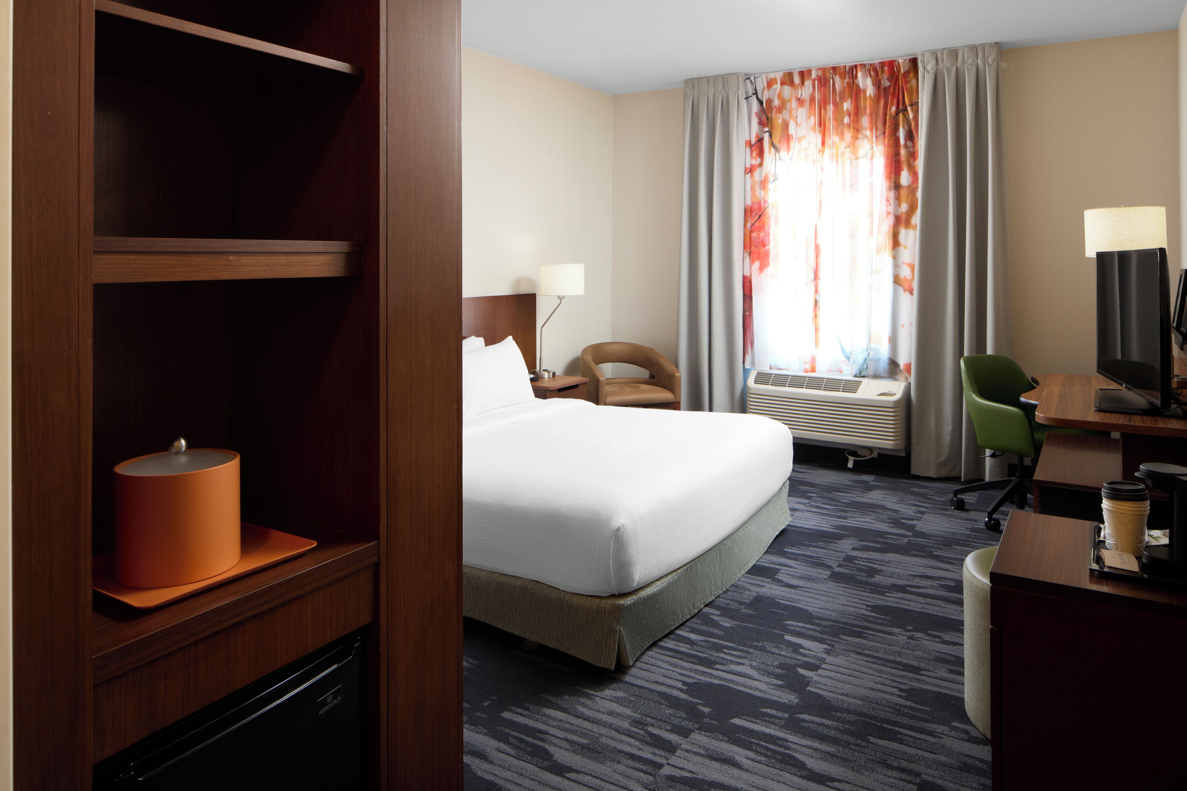 A hotel room with a bed, a desk, a chair, a lamp, a heater, and a window with curtains.