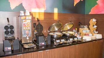A buffet counter with various food items and appliances, including a waffle maker and a coffee machine.