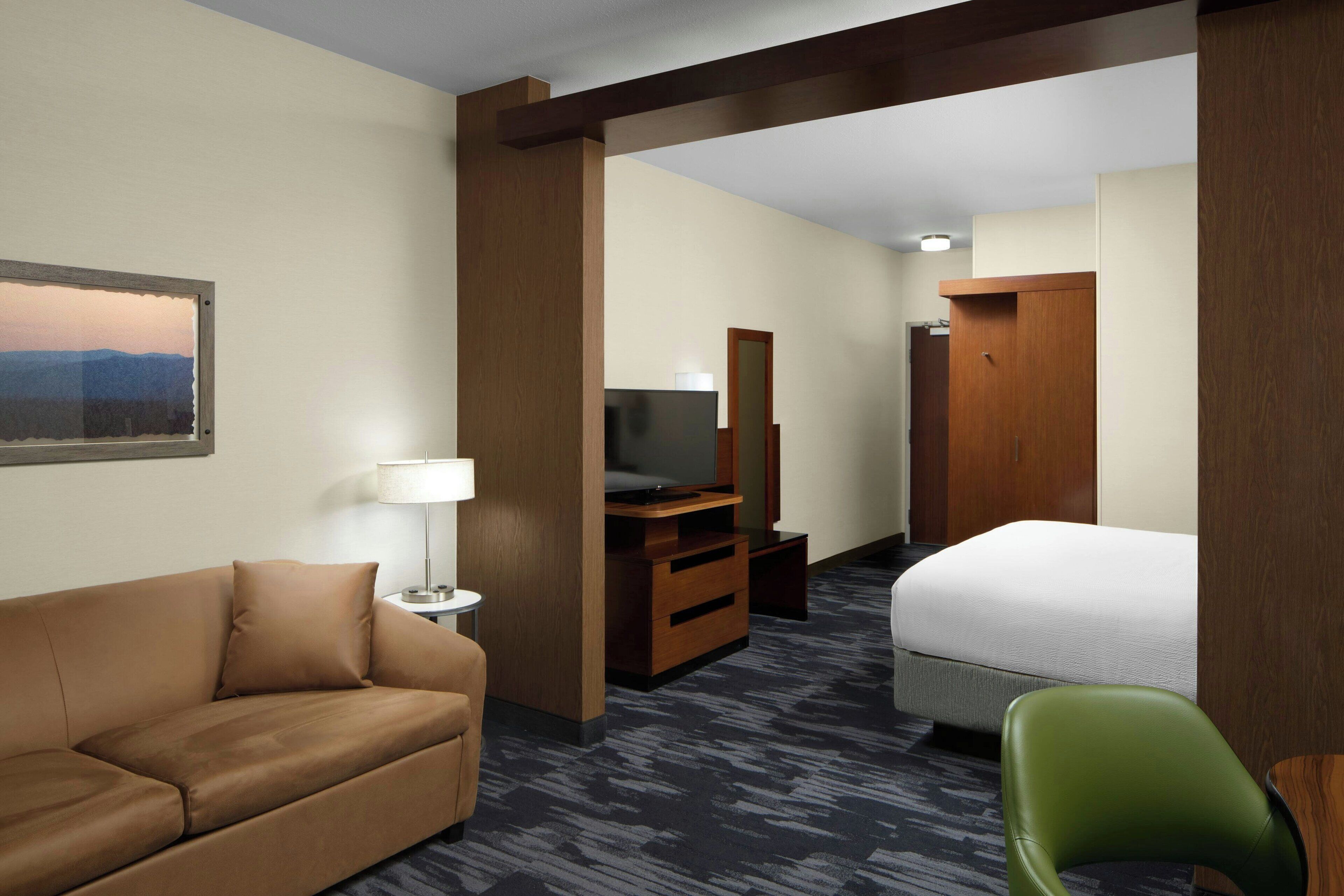 A hotel room with a sofa, a bed, a television, a mirror, and a desk.