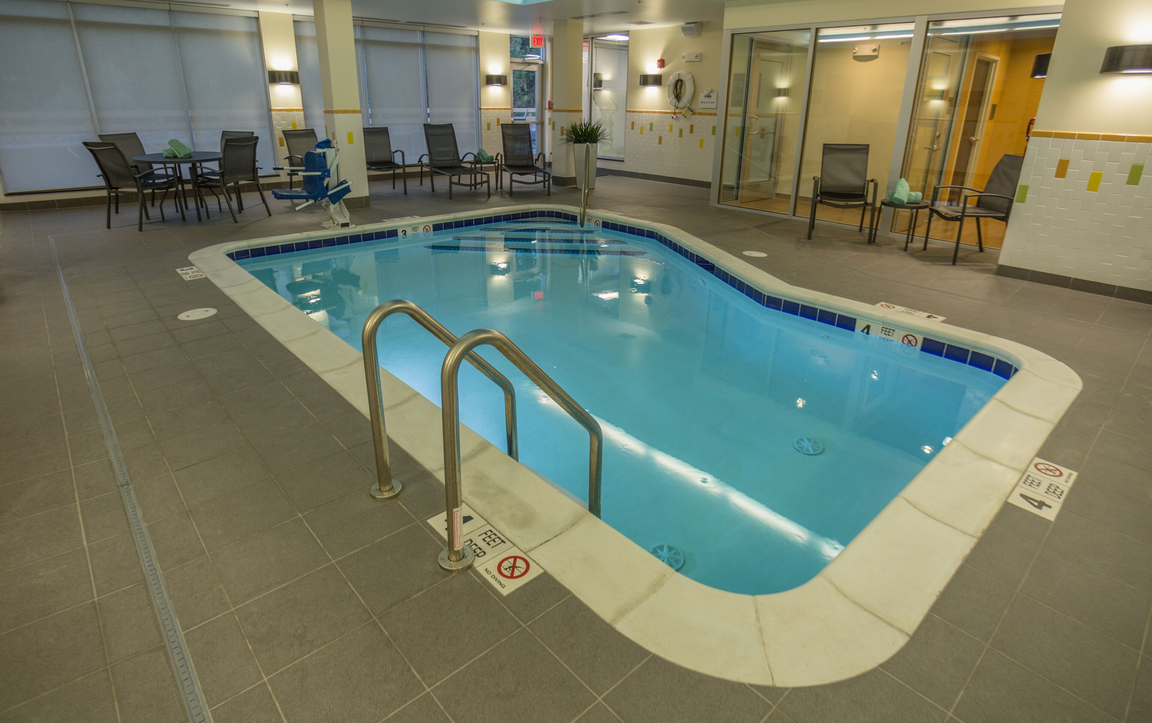 Une piscine intérieure équipée d’un escalier, de chaises et d’un sol carrelé.