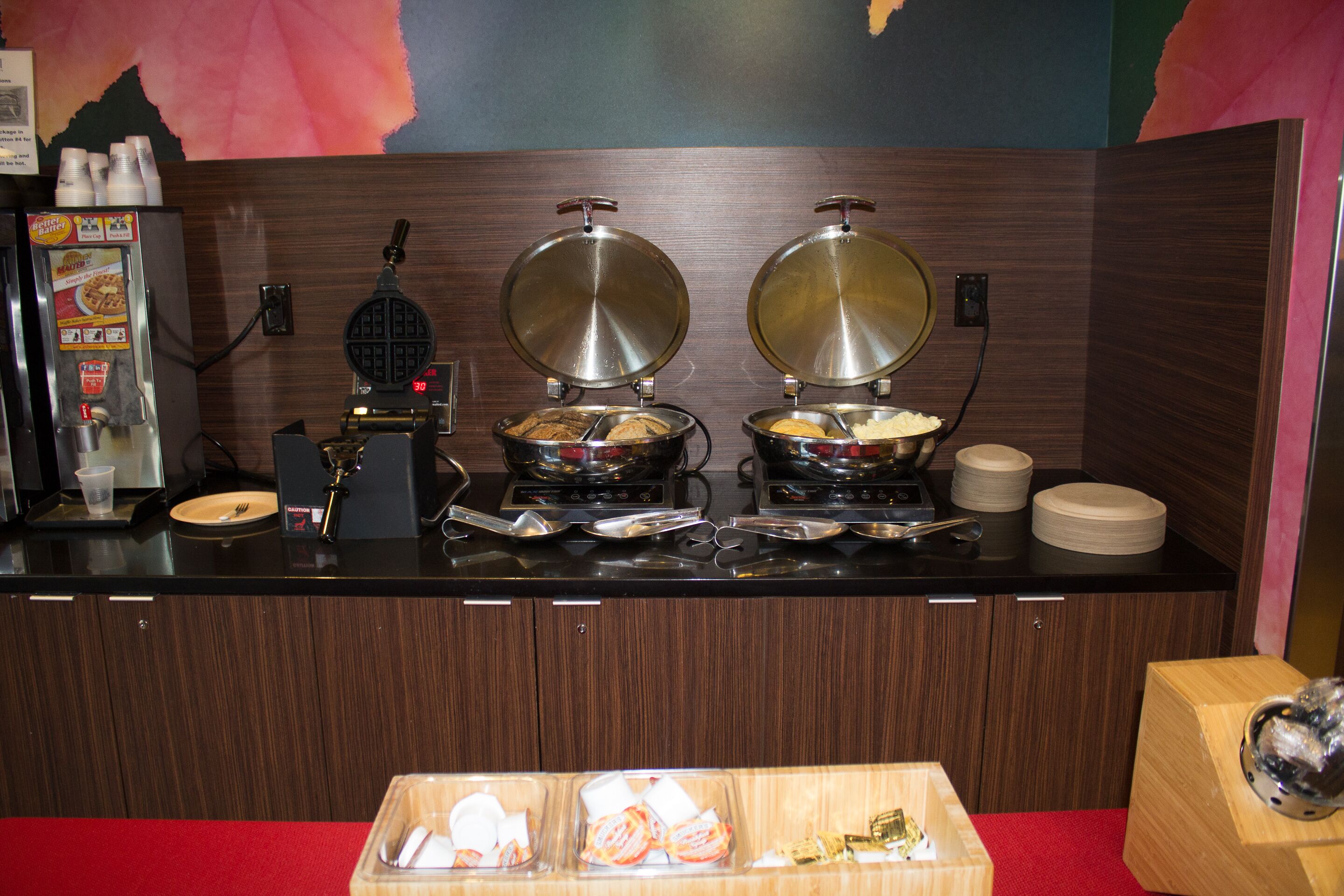 Un buffet avec deux gaufriers, une machine à café et divers récipients pour les aliments.