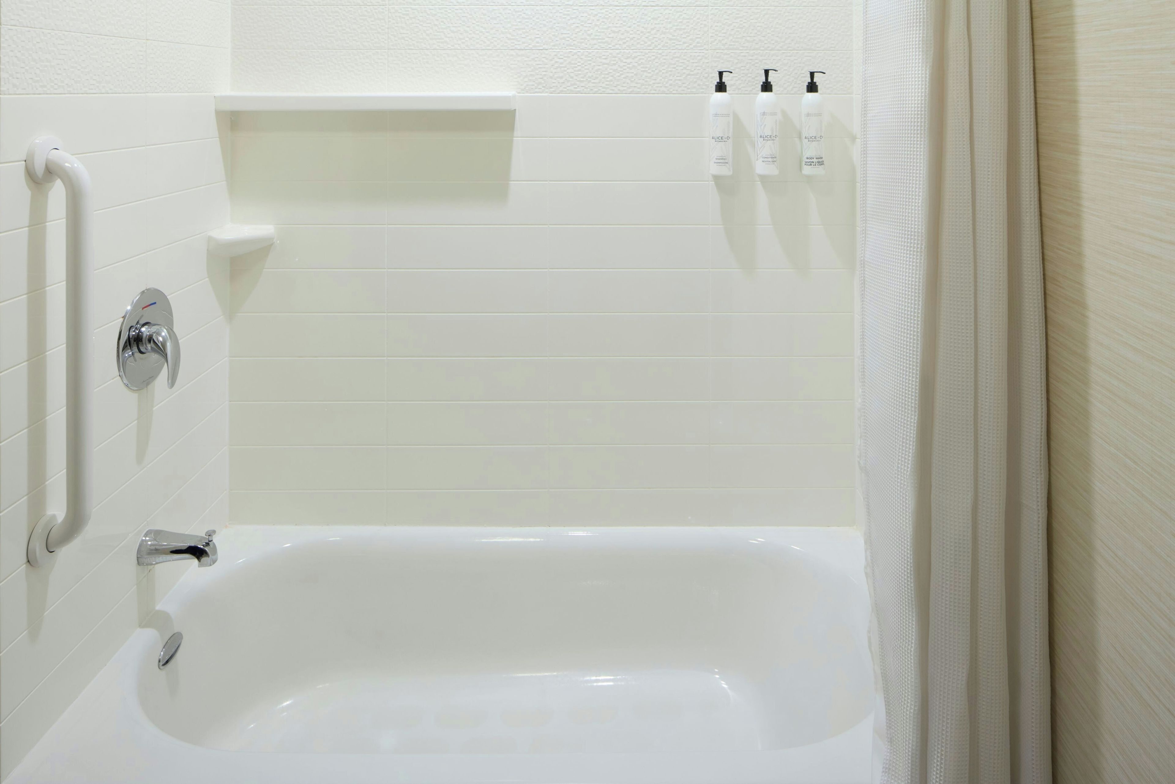 A white bathtub with a chrome faucet, a shelf above it, and three bottles of toiletries.