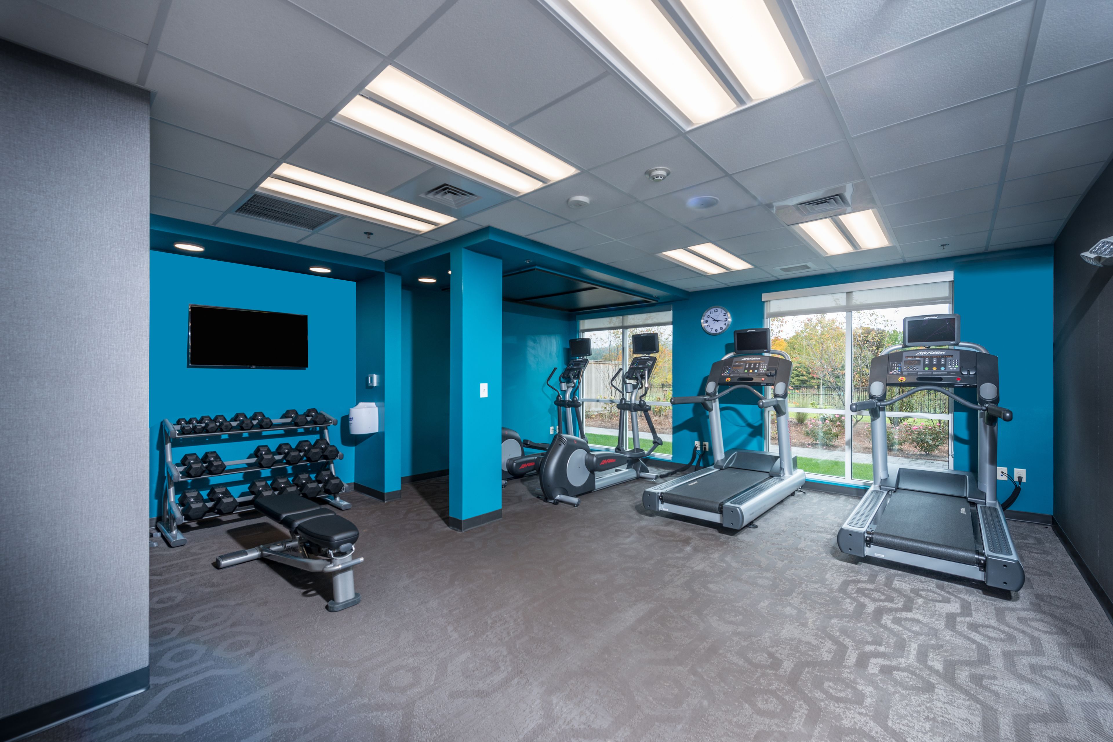 Un gimnasio con cintas de correr, elípticas y una prensa de banca.