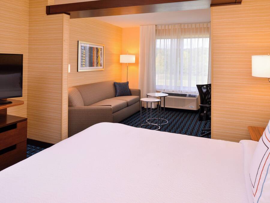 A hotel room with a large bed, a sofa, a small table, a TV, and a window with curtains.