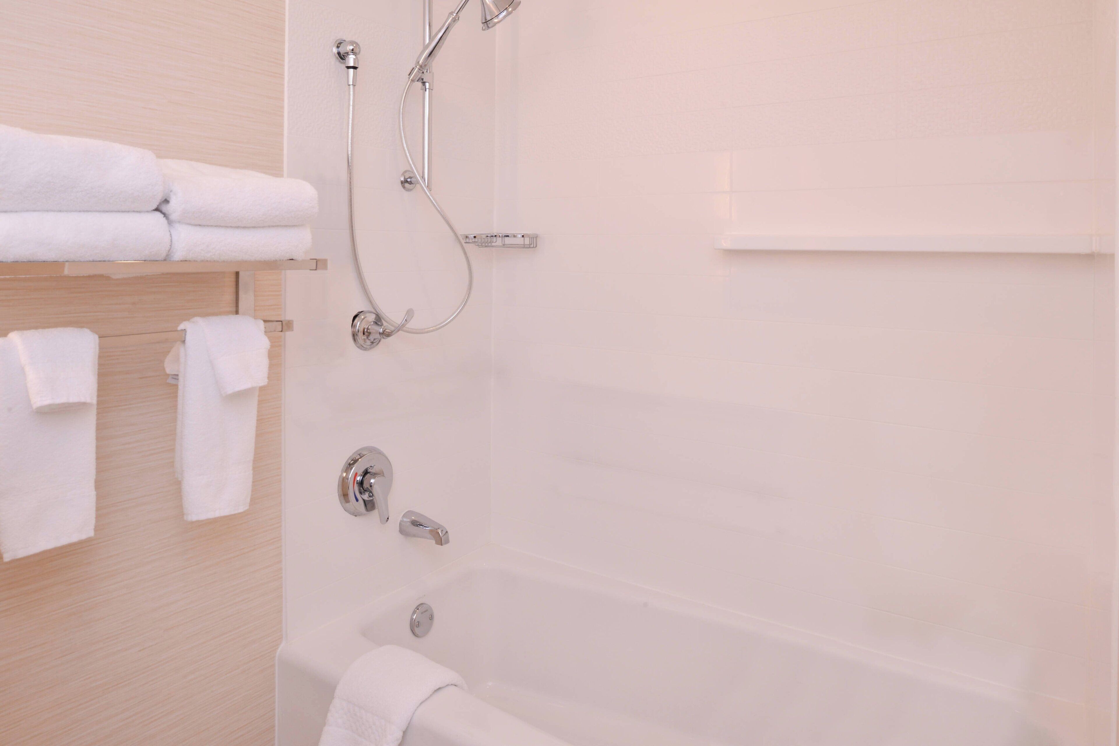 A bathroom with a bathtub, a shower, and a towel rack with folded towels.