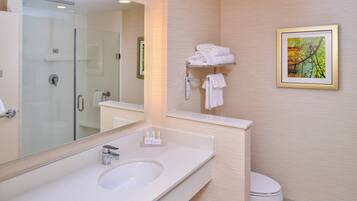 Une salle de bain moderne avec une douche à parois de verre, un lavabo blanc et des toilettes. Un tableau encadré est accroché au mur, et un porte-serviettes contient des serviettes pliées.