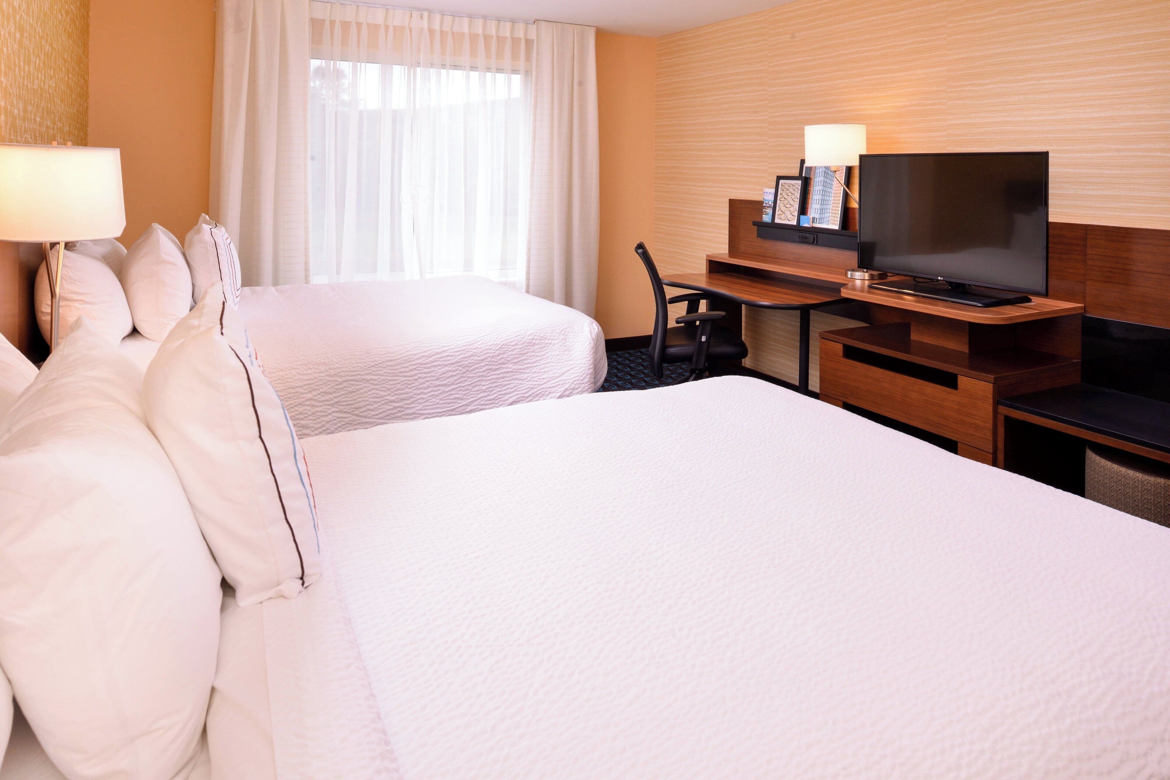 A hotel room with two beds, a desk with a TV, and a lamp.