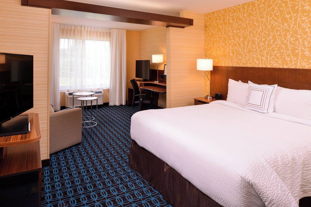 A hotel room with a large bed, a desk with a chair, a television, and a small table with a lamp.