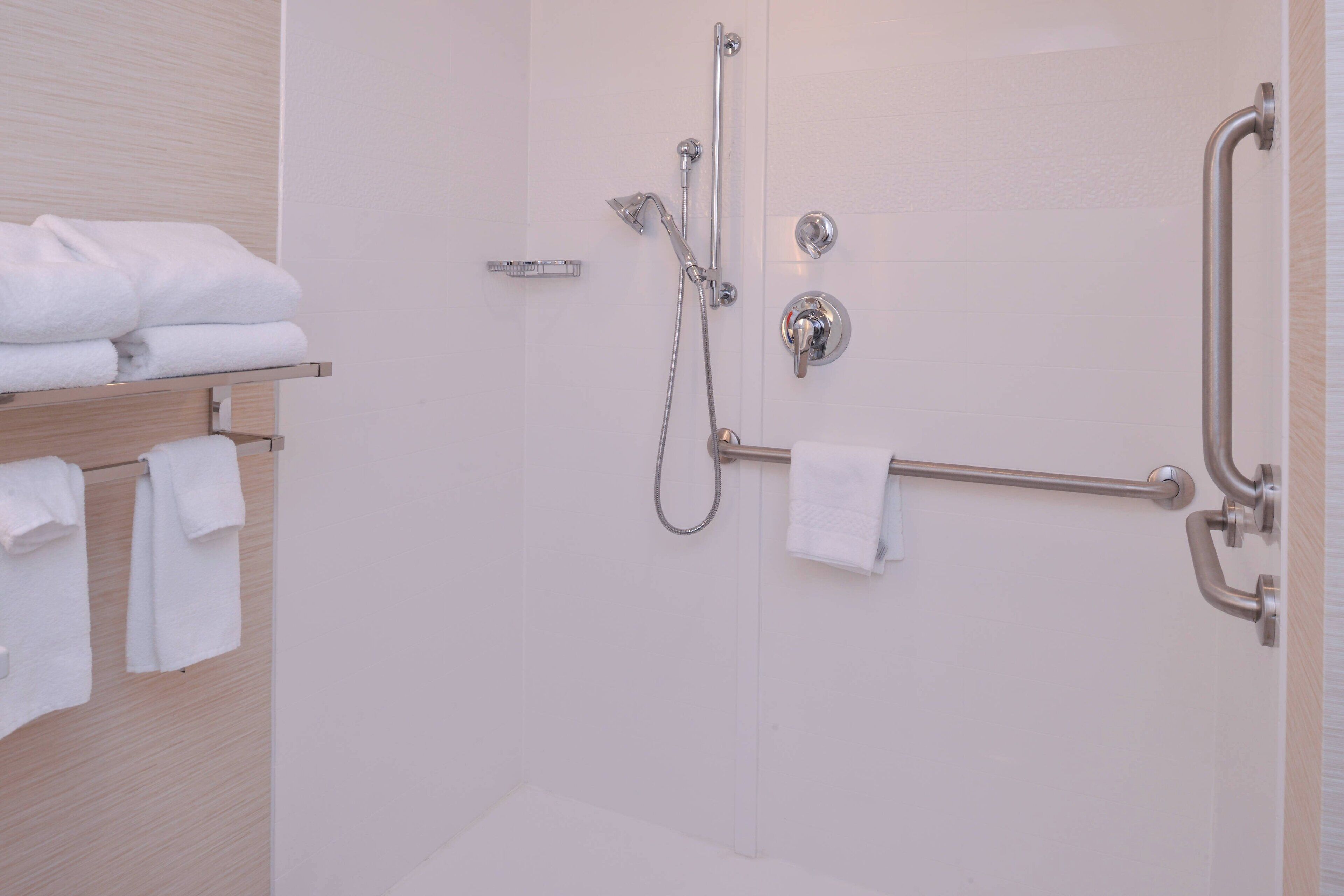 Baño con ducha, barras de apoyo y un perchero con toallas dobladas.