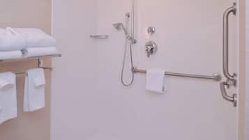 Baño con ducha, barras de apoyo y un perchero con toallas dobladas.