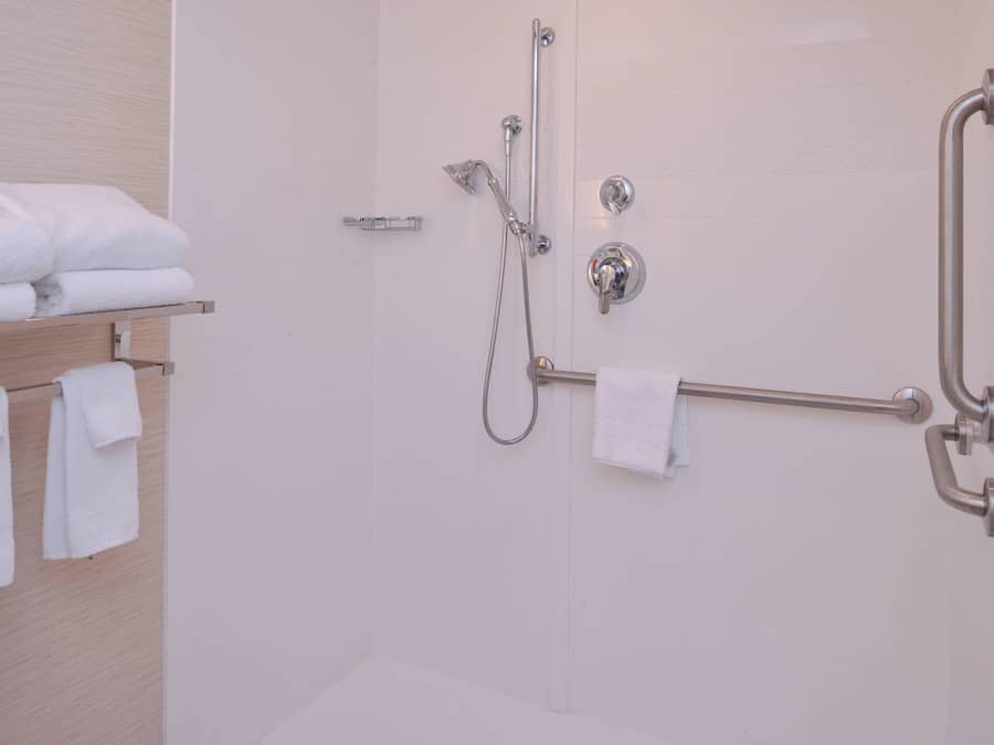 Baño con ducha, barras de apoyo y un perchero con toallas dobladas.