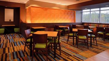 A restaurant with booths and tables, patterned carpet, and a view of trees through large windows.