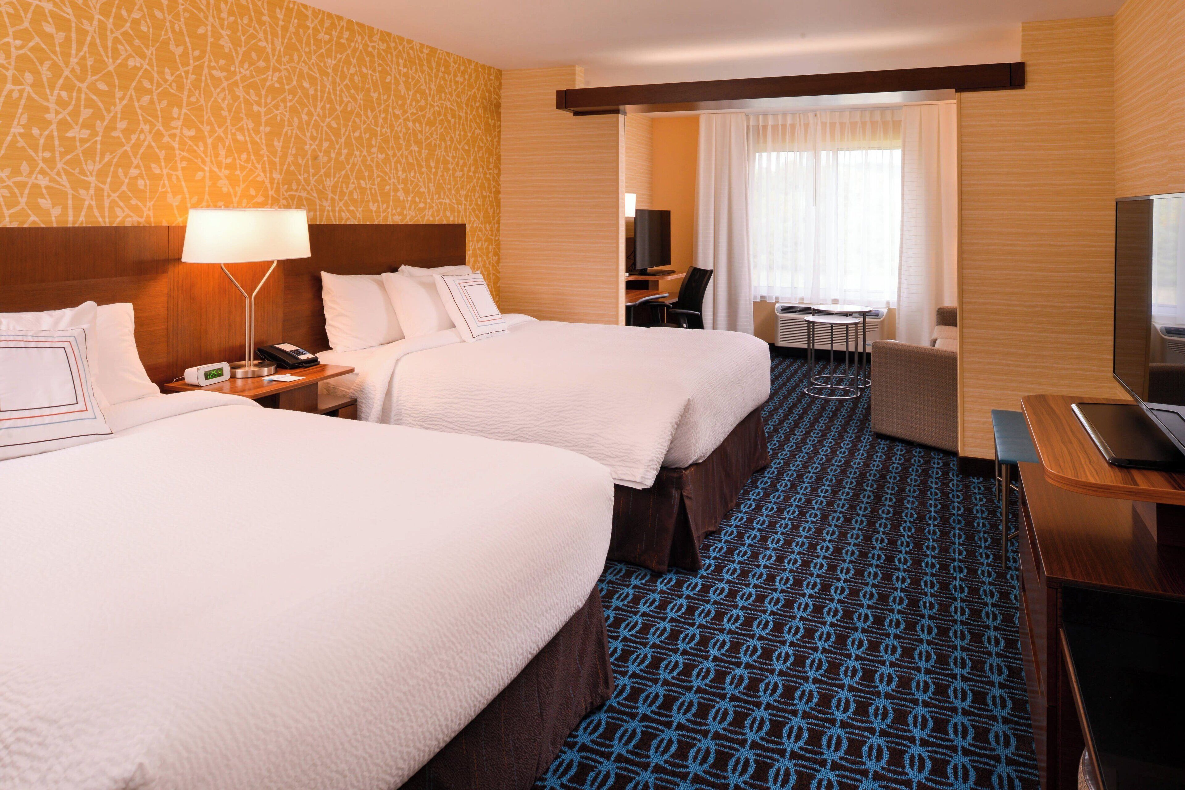 Hotelkamer met twee bedden, een bureau met een laptop, een televisie en een zithoekje met een stoel en een tafeltje.