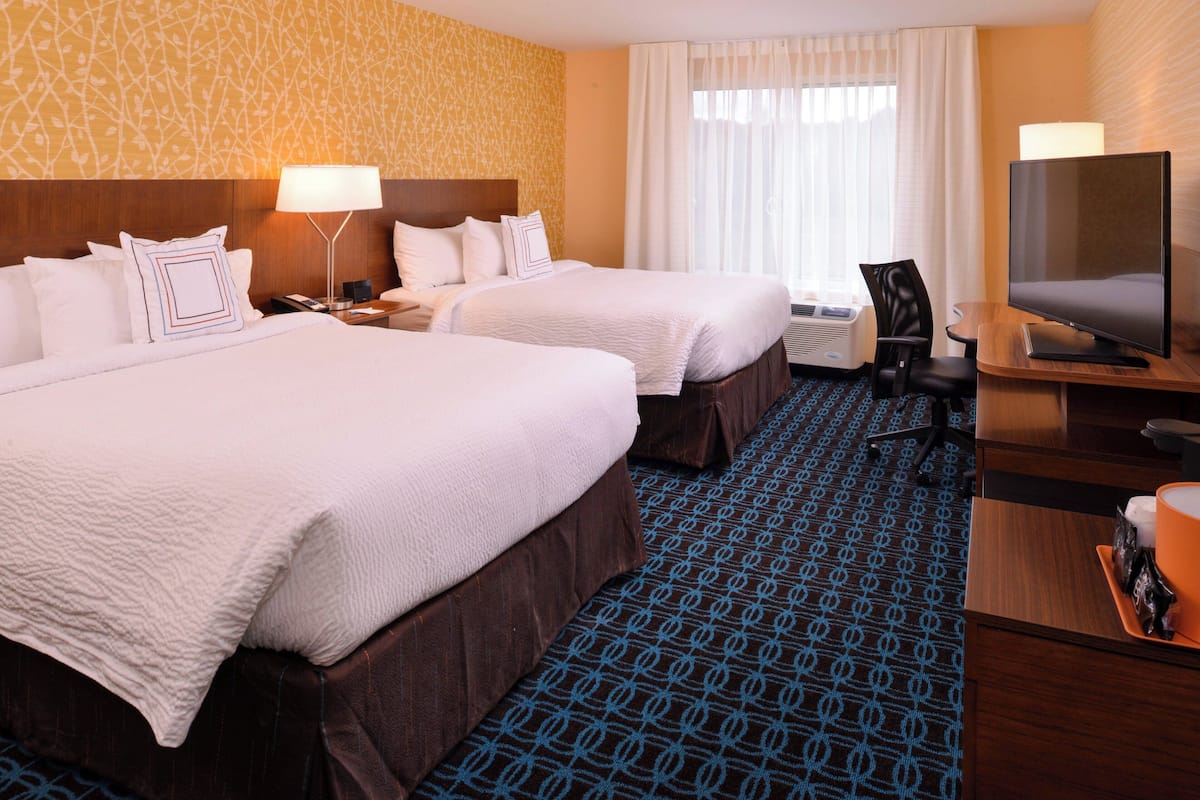 A hotel room with two beds, a TV, a desk, and a chair.