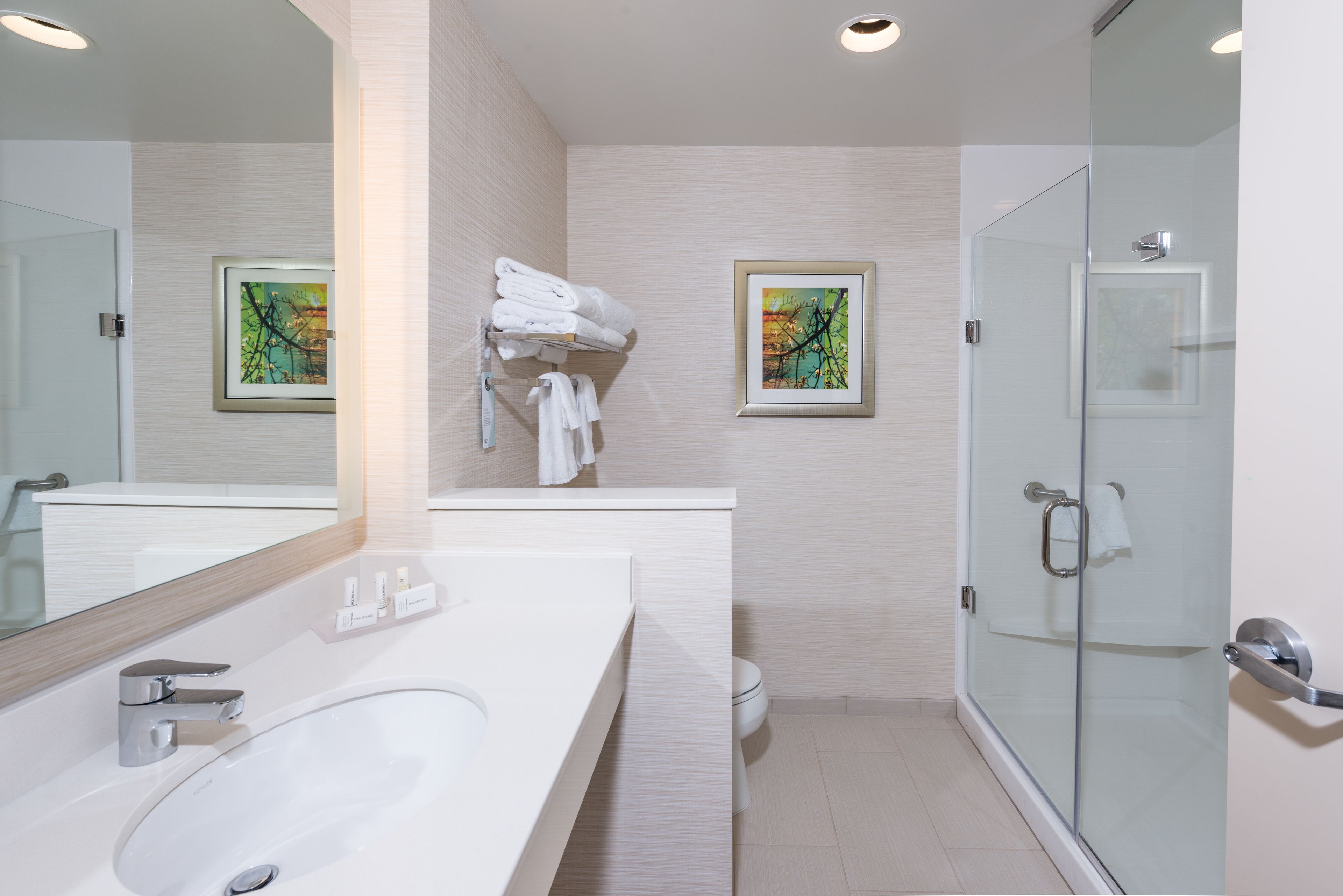 Un baño moderno con un espejo grande, lavabo blanco y cabina de ducha con paredes de vidrio.