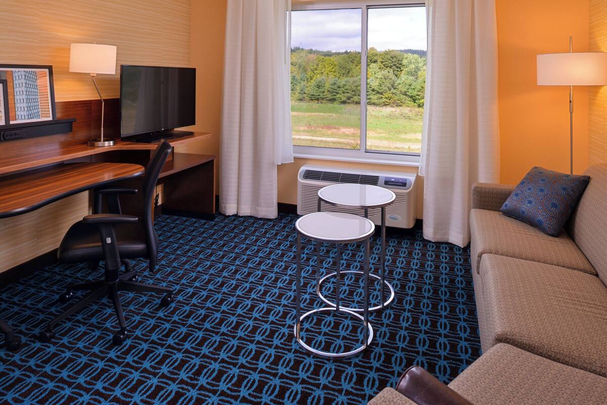 A hotel room with a desk, chair, TV, small round table, and a sofa.