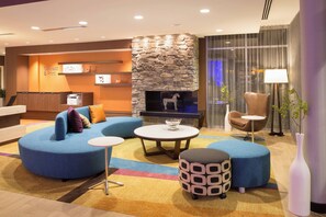 A modern lobby with a stone fireplace, blue seating, a round table, and a reception desk. - Fairfield Inn & Suites by Marriott Burlington (Burlington)