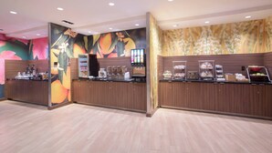 Un espace d’accueil moderne avec un comptoir en bois, un kiosque numérique et un présentoir de fruits.