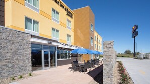 L’extérieur d’un hôtel avec une façade en pierre, de grandes fenêtres et un espace extérieur aménagé avec des parasols bleus.