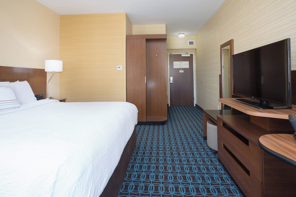 A hotel room with a bed, a desk with a flat-screen TV, a mirror, and a patterned carpet.