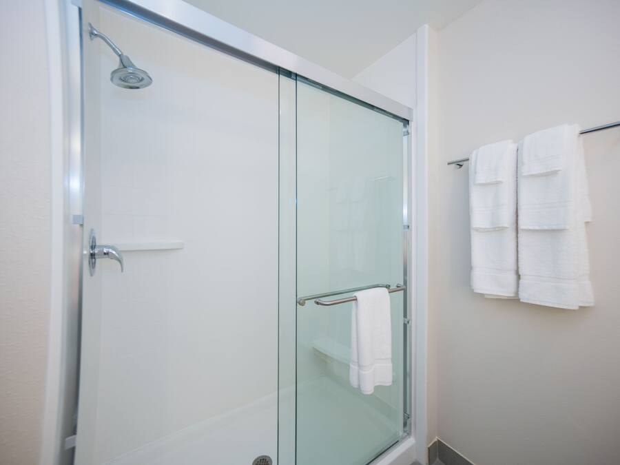 Une douche fermée par des parois en verre, dotée d’un pommeau de douche à main, d’une porte en verre et d’un porte-serviettes avec deux serviettes.