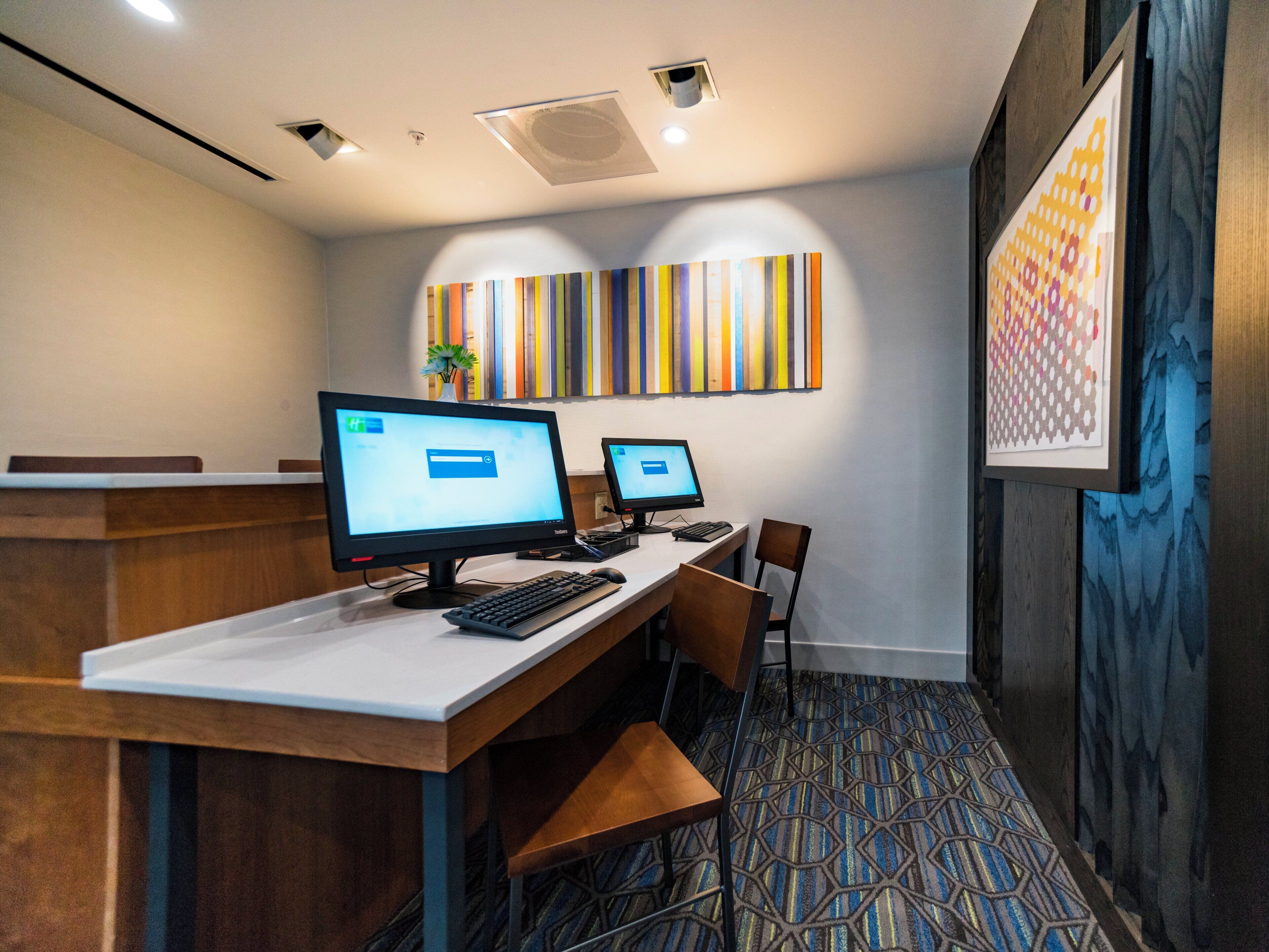 Um espaço de escritório moderno com dois computadores, uma mesa de recepção e um tapete estampado.