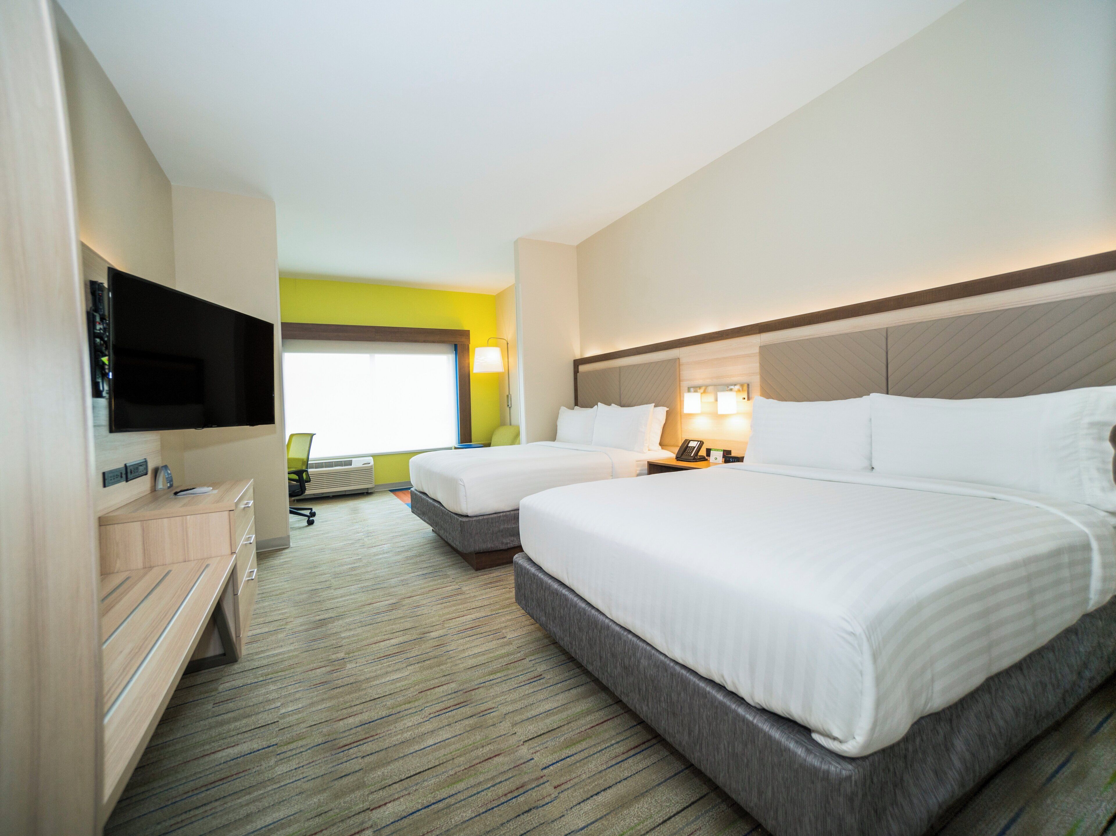 A hotel room with two beds, a flat-screen TV, a desk with a chair, and a window with a view.