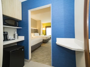 Quarto de hotel com cama, escrivaninha com micro-ondas, cafeteira e lixeira.