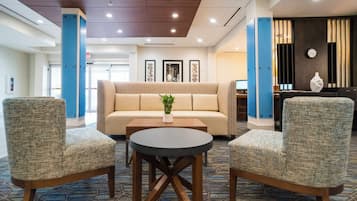 A hotel lobby with a sofa, two armchairs, a coffee table, and a reception desk.
