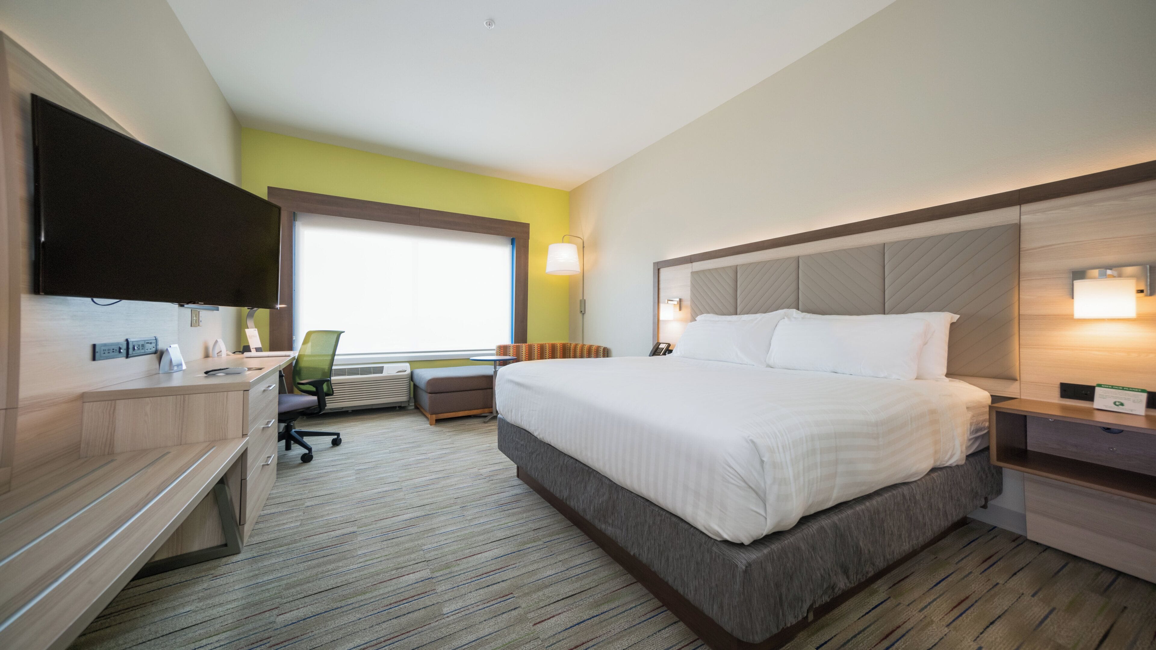 A hotel room with a bed, desk, chair, and a television.